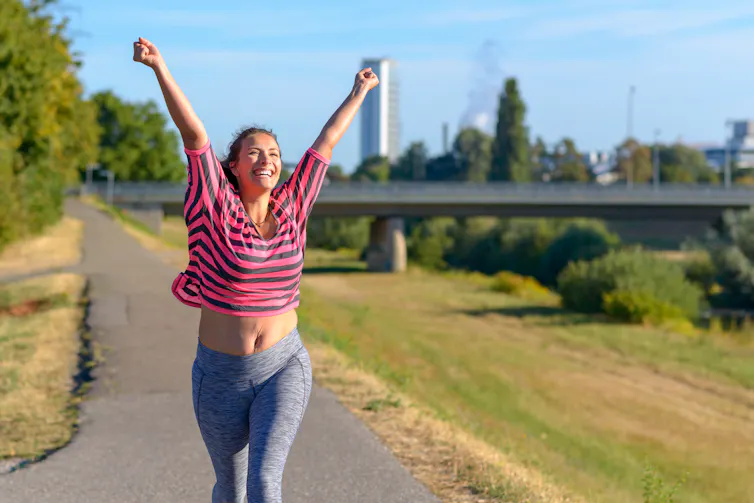 A woman in fitness clothes running with her arms in the air