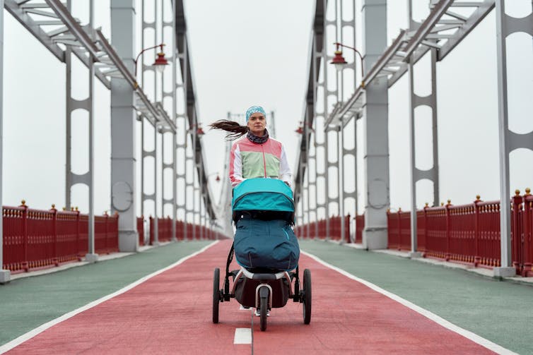 A woman with a ponytail jogging on a bridge with a blue stroller