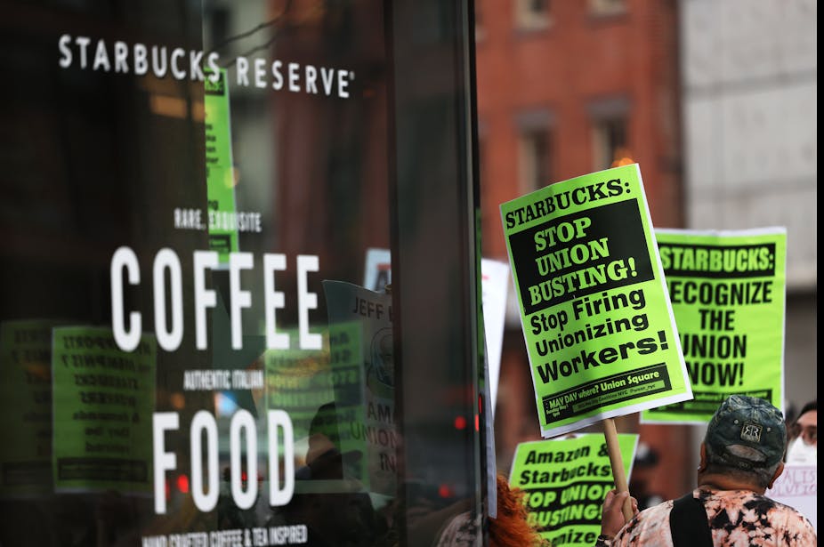 People hold signs saying 'Starbucks: Stop Union Busting' outside a Starbucks store.