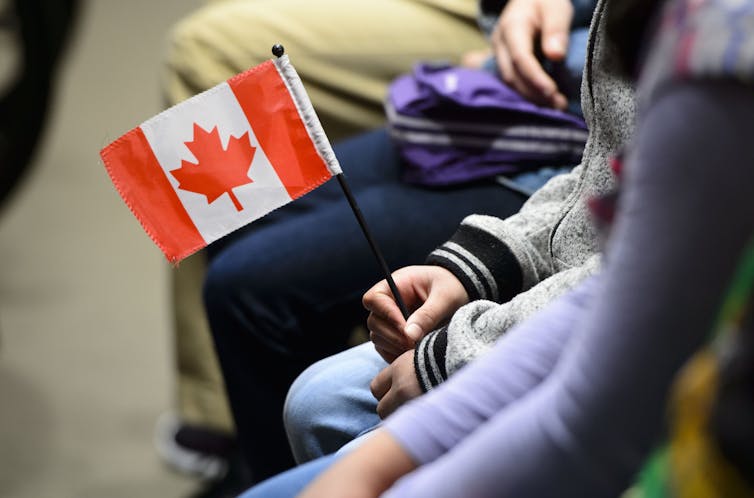 The hands of a person are seen holding a small Canadian flag.