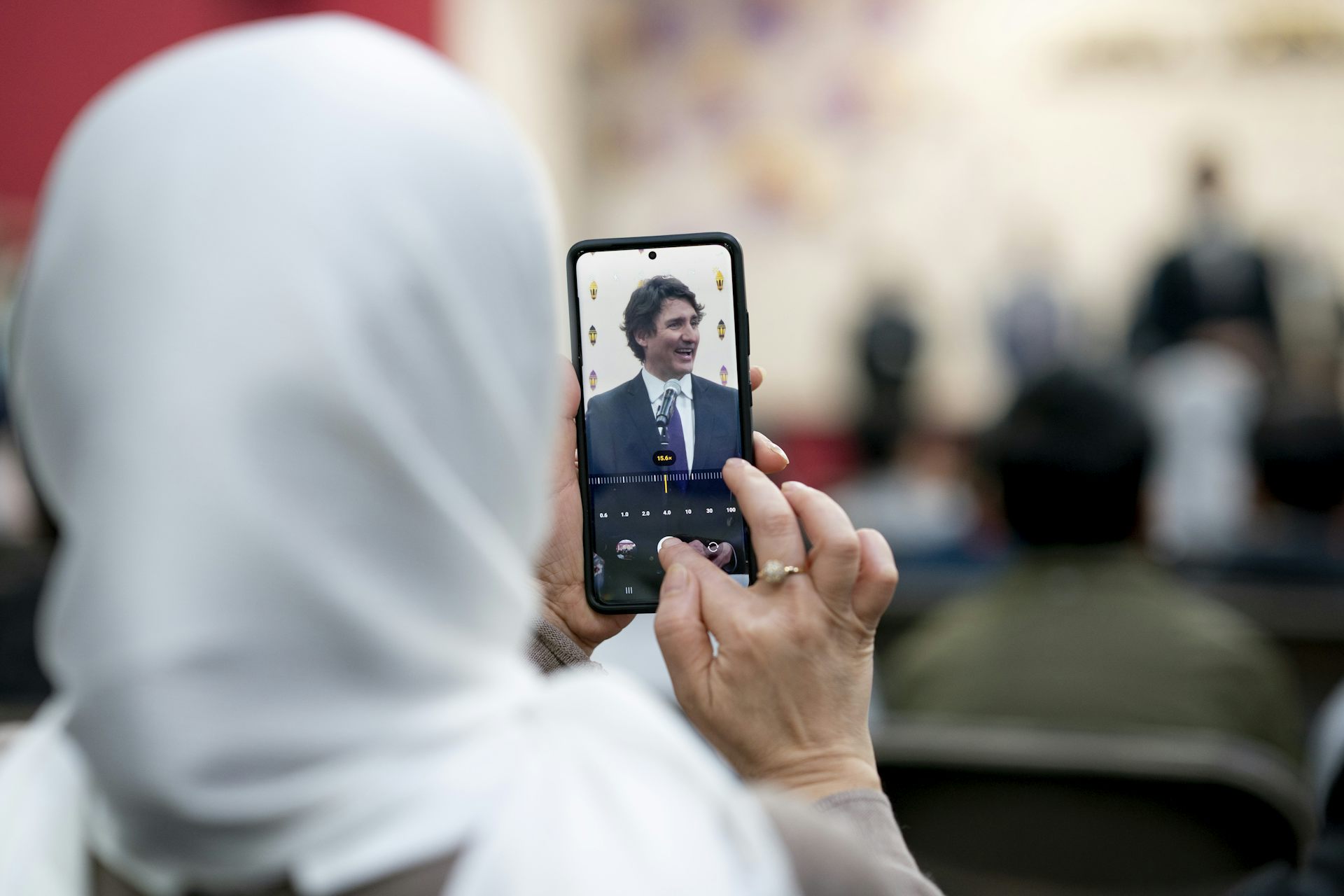 A woman in a white hijab adjusts the settings of her smartphone while capturing an image of a man with dark hair
