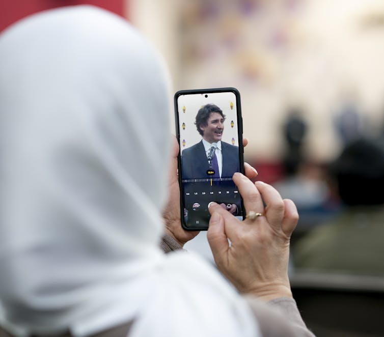 A woman wearing a white veil adjusts her smartphone settings while taking a picture of a man with dark hair