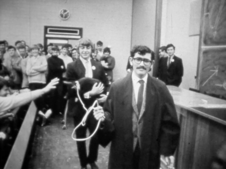 Boy in university robes leads a pig on a leash