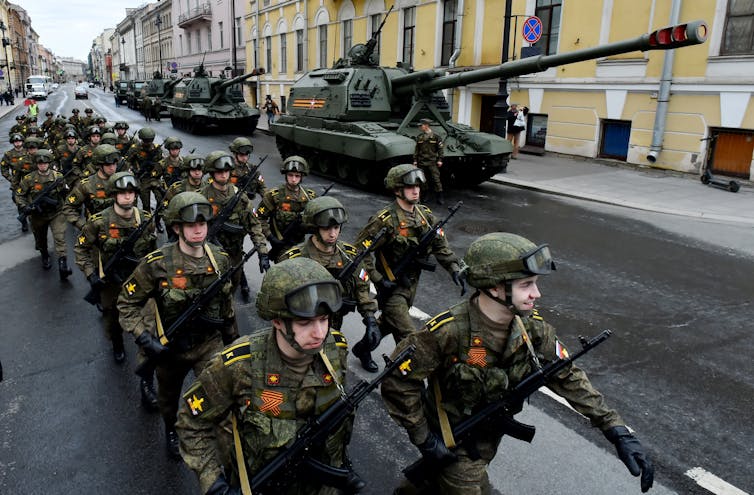 military cadets march next to tanks