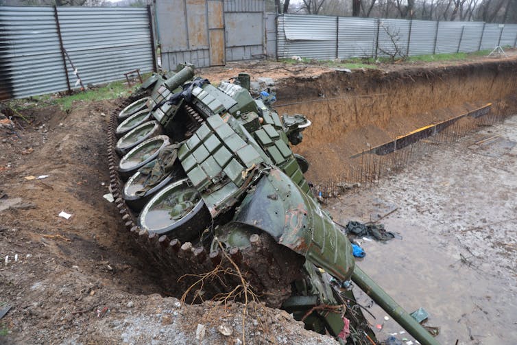 A damaged Russian tank is seen on its side in a ditch.