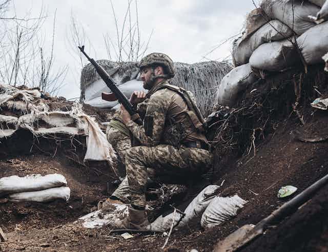 A Ukrainian soldier checks his rifle while on guard in a trench.
