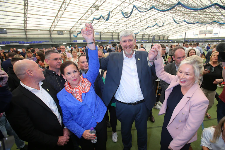 Man and two woman hold hands in air and smile in front of crowd.