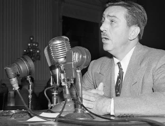 Man speaks before mutliple microphones during a hearing.