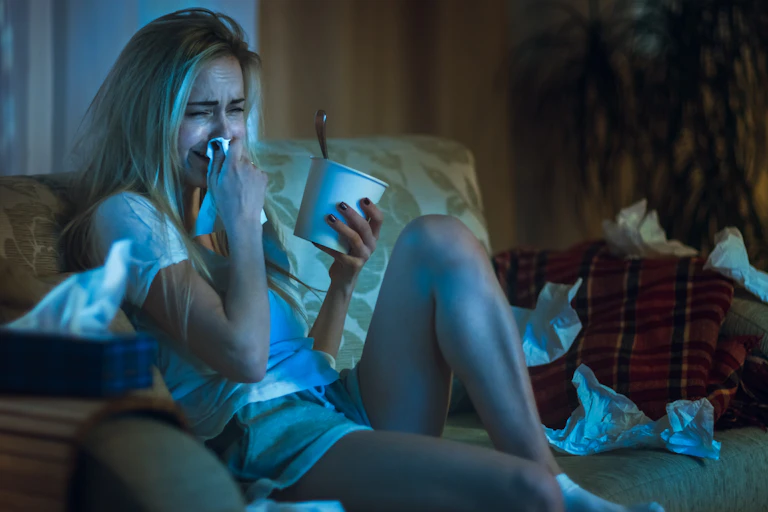 Heartbroken Girl Sitting on a Sofa, Crying, Using Tissues, Eating Ice Cream and Watching Drama on TV.