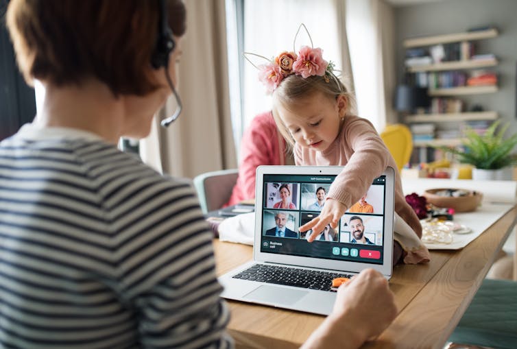 Woman speaks on the computer while child leans over and touches screen.