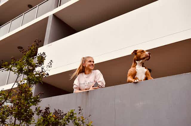 woman and dog look from apartment balcony 