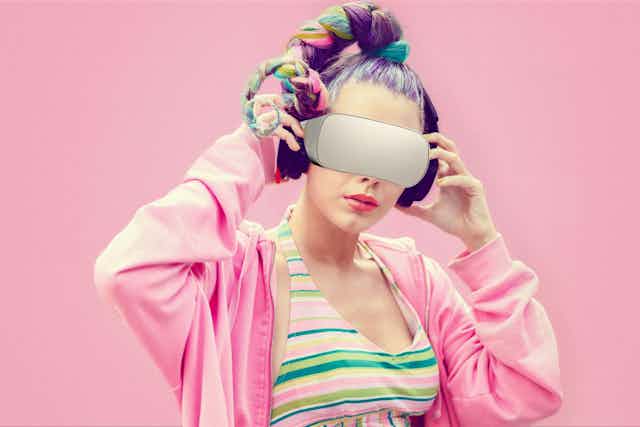 A young woman with multicoloured hair and a pink hoodie wears a VR headset.