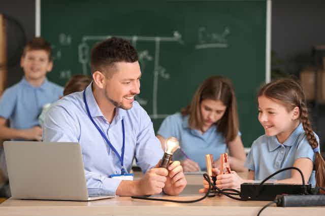 Girls and teacher in physics class with lightbulb