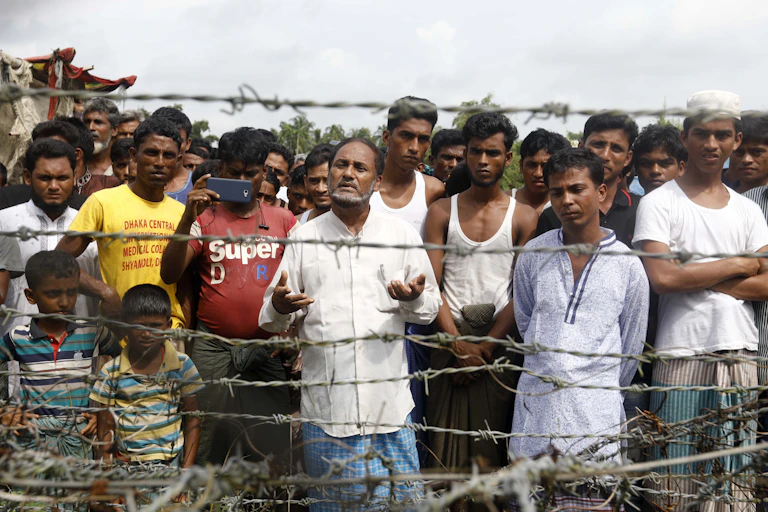 A group of Rohingya men and boys standing behind a barbed wire fence.