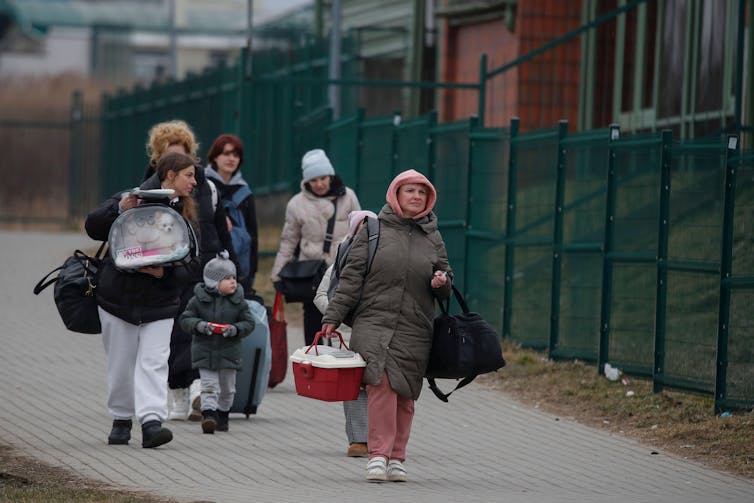 Several Ukrainian adults and a child, wearing winter clothes and walking while carrying bags and pet carriers.