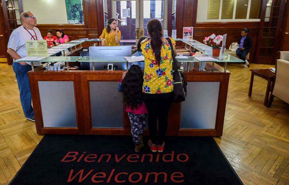 A woman and a child stand on a mat saying 'welcom' and 'bienvenido' in an office.