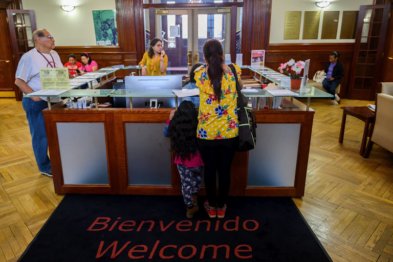 A woman and a child stand on a mat saying 'welcom' and 'bienvenido' in an office.
