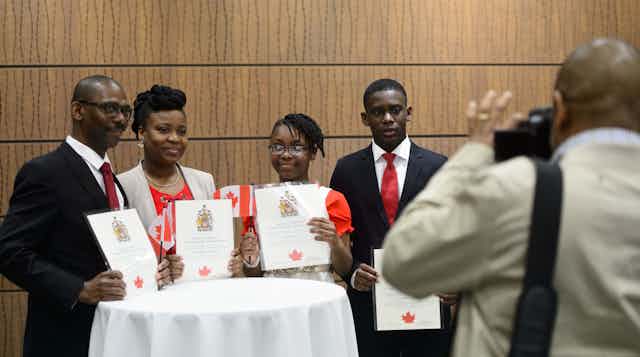 A Black family smiles for a photo while holding their Canadian citizenship certificates.