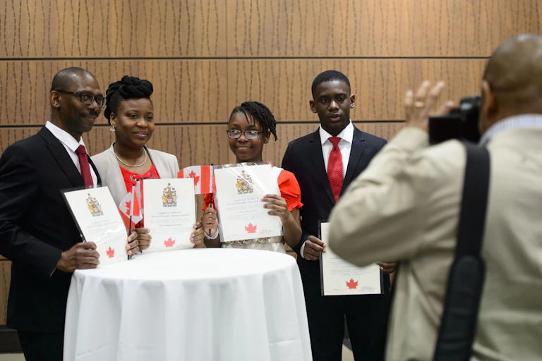 A Black family smiles for a photo while holding their Canadian citizenship certificates.