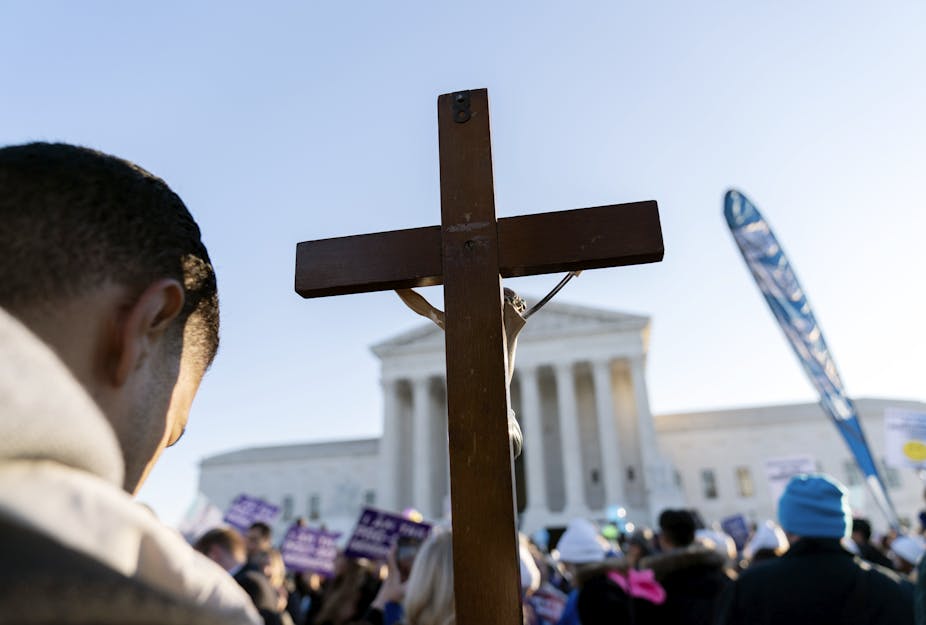 A man bows his head while raising the cross in front of the US Supreme Court.