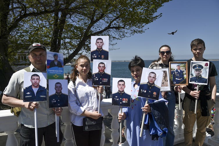 A group of people hold photos of soldiers.