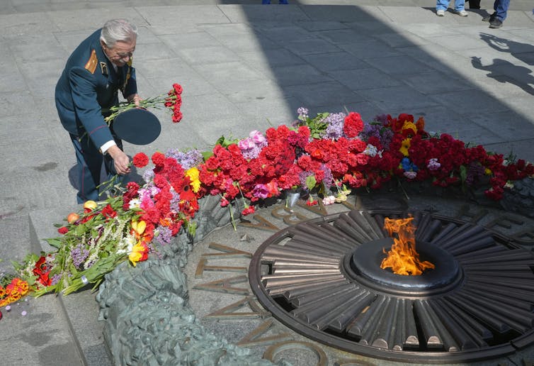 A man in military uniform is seen laying flowers in front of a flame.