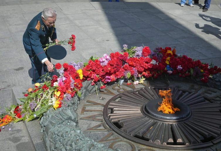 A man in military uniform is seen laying flowers in front of a flame.
