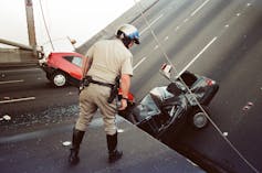 A police officer looks over the edge of a section of the bridge to cars below.