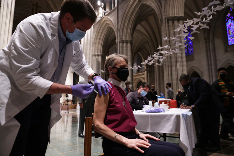 A health care worker with a face mask giving a vaccine to a woman.