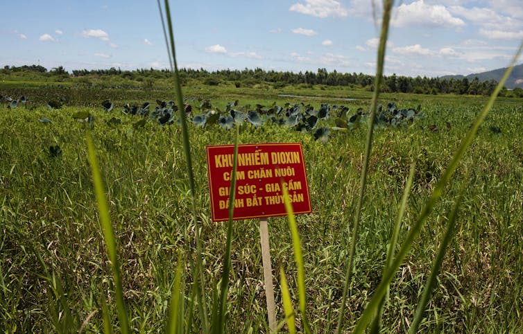 A sign that reads 'Dioxin contamination zone — livestock, poultry and fishery operations not permitted' is placed in a field.