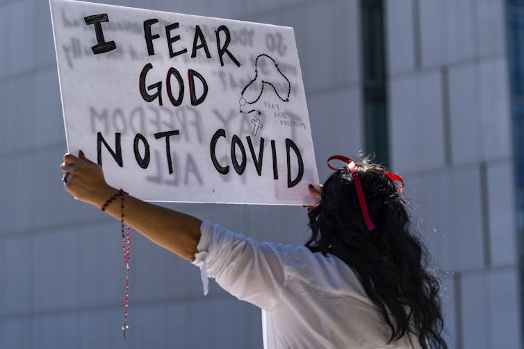A woman in a white shirt, holding a sign saying 'I fear God, not COVID.'