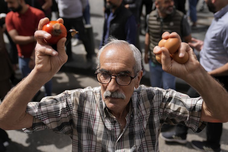 Un hombre sostiene fruta en sus manos, protestando.