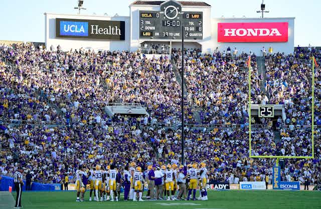 A crowd in a stadium watch football players on a field