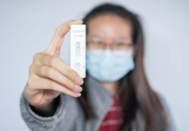 A woman holds up a rapid antigen test pad to show she tested negative.