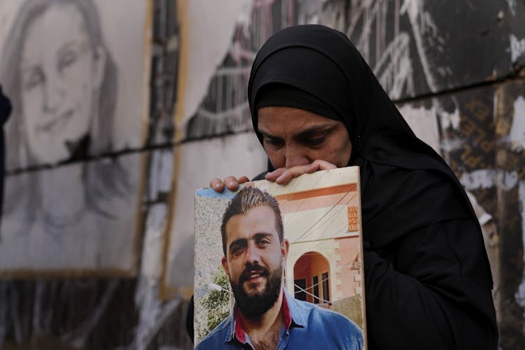 Une mère dont le fils a été tué lors de l’explosion survenue en août 2020 dans le port maritime de Beyrouth tient un portrait de ce dernier lors d’un rassemblement, le 4 avril 2022, pour marquer les vingt mois écoulés depuis la tragédie. (AP Photo/Hussein Malla)