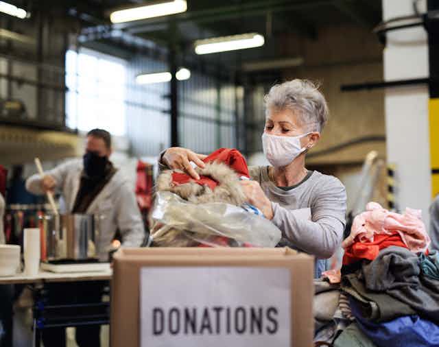 A woman in a mask packing clothes in a bag to be donated.