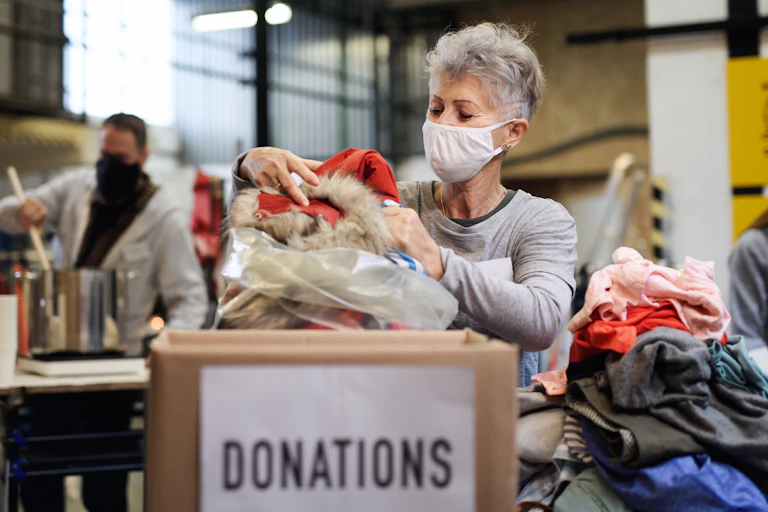 A woman in a mask packing clothes in a bag to be donated.