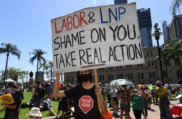 A protester in a Stop Adani shirt holds up a sign saying 'Labor & LNP Shame on you take real action' 