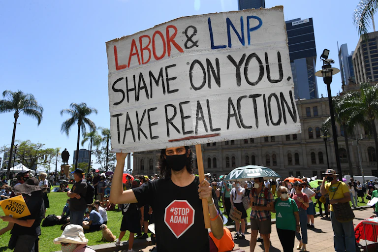 A protester in a Stop Adani shirt holds up a sign saying 'Labor & LNP Shame on you take real action'