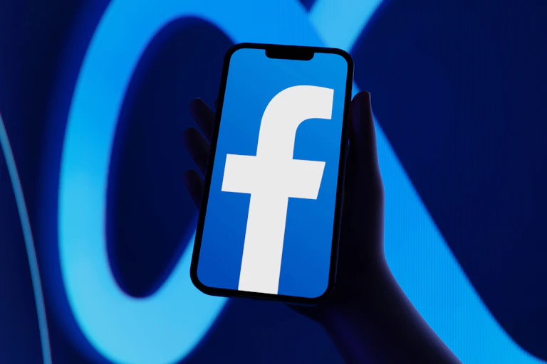 Facebook logo on a phone, held in front of a larger background with Meta's logo resembling an infinity loop