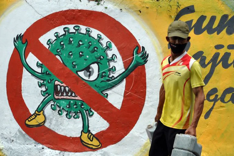 A man uses face mask when walking in front of a moral of COVID-19 virus in Bogor, West Java, Indonesia.