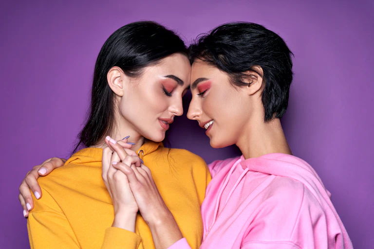 two women in bright clothes clasping hands, looking lovingly at each other