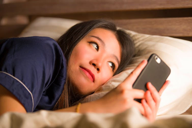 woman in bed looking at phone and smiling