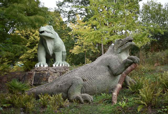 Two large green statues of dinosaurs surrounded by trees