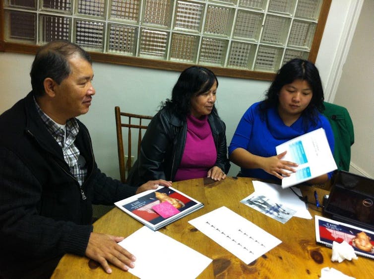 A man and two women sit at a table where health information, checklists and other papers are spread out.