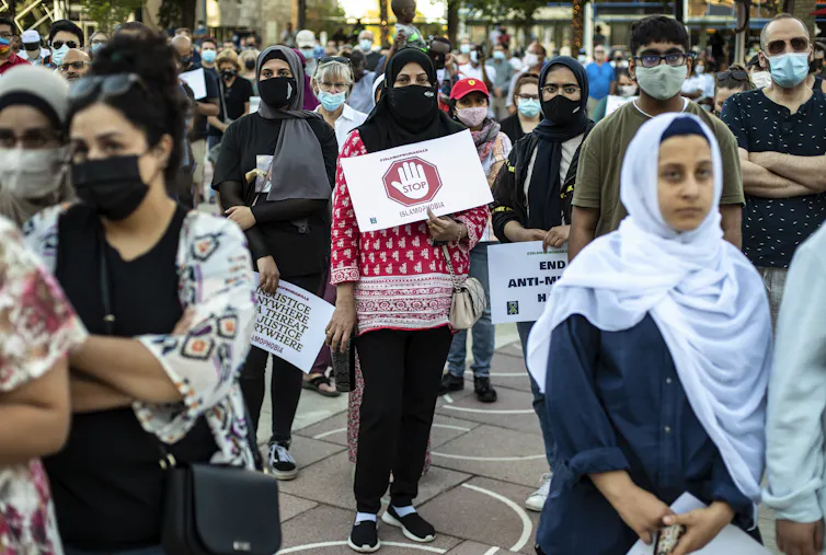 At the centre of the image are three women wearing the hijab holding placards and protesting against the rising Islamophobia in Canada