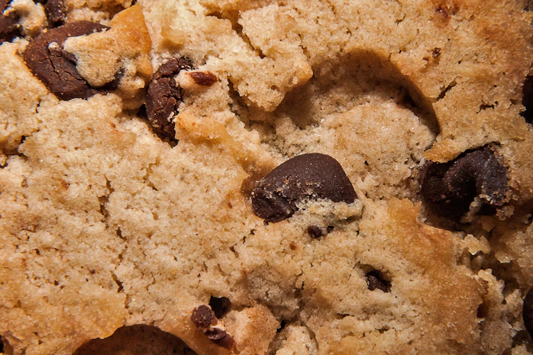 closeup of the golden brown surface of a chocolate chip cookie with dark brown and melted chocolate chips here and there