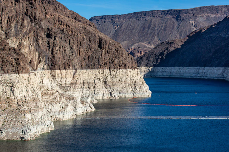 A lake surrounded by brown rock cliffs that turn white well above the water line