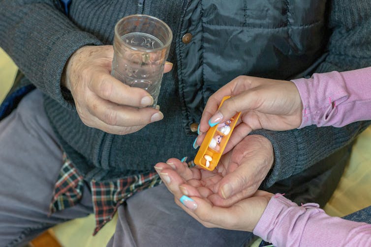 Older man holding a glass of water takes tablets in his hands.