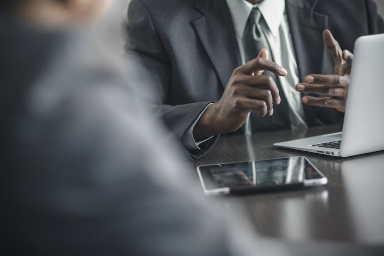 A person in a suit sits with a laptop and a mobile phone.